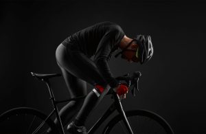 Man cycling a black bicycle in black gear with a black background