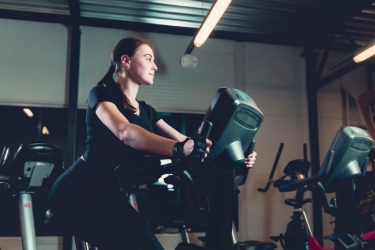 Woman using stationary cycle in a gym illustrating class guide on CicloZone, an indoor cycling app